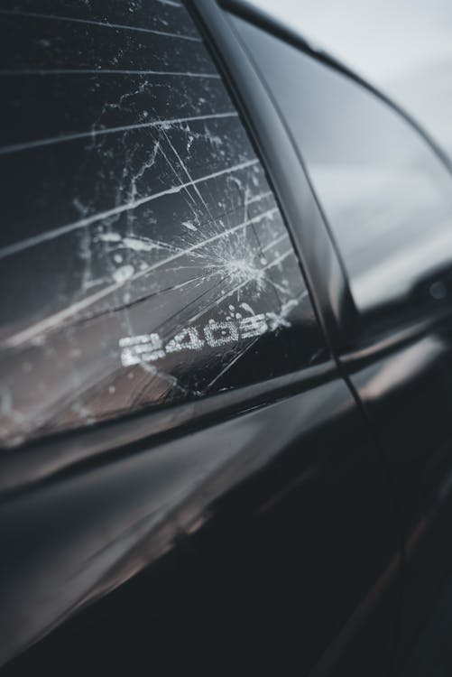 Close-up of car window glass with spreading cracks showing auto glass damage requiring repair