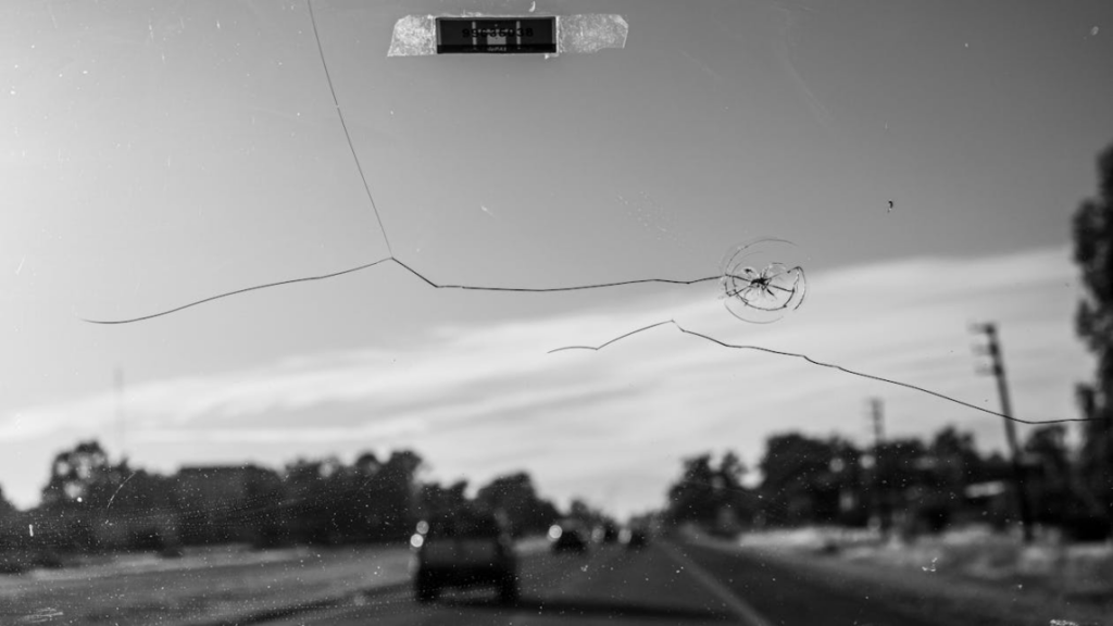 Cracked car windshield showing road damage and spreading impact lines on the glass