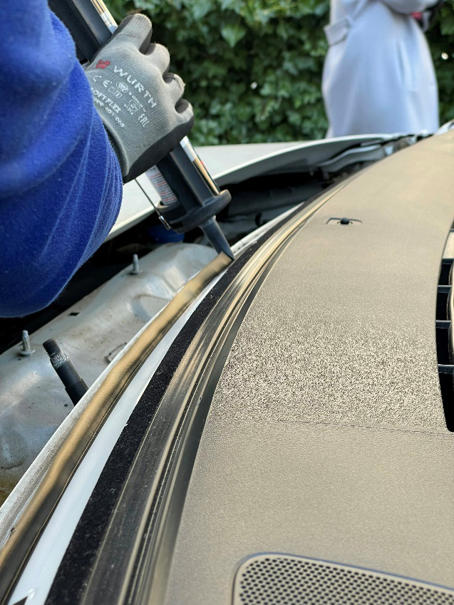 Auto glass technician applying adhesive for windshield replacement installation